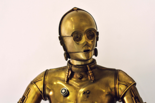 A foto mostra o robô C3PO, da franquia Star Wars. Trata-se de um robô alto, esguio, com a lataria dourada. Faz referência a um robô amigo, como uma automação bem-vinda a cooperar com os seres humanos.