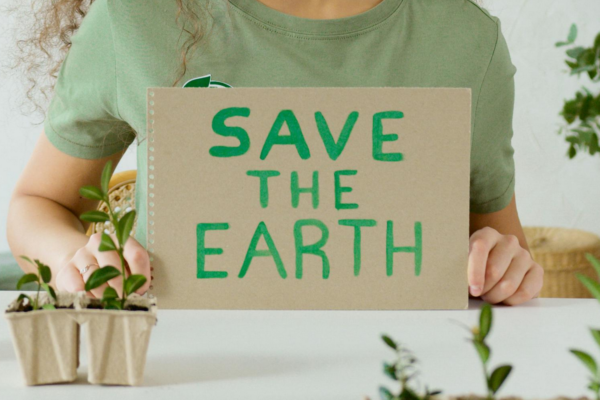 A imagem foca em uma pessoa segurando uma placa de papelão escrita "save the Earth", em tradução livre: "salve o planeta", fazendo referência ao marketing verde e seu impacto ambiental.