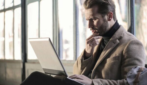 A imagem mostra um homem branco com o cabelo curto, olhando o notebook em sua frente, sobre seu colo. Ele veste uma jaqueta grossa.